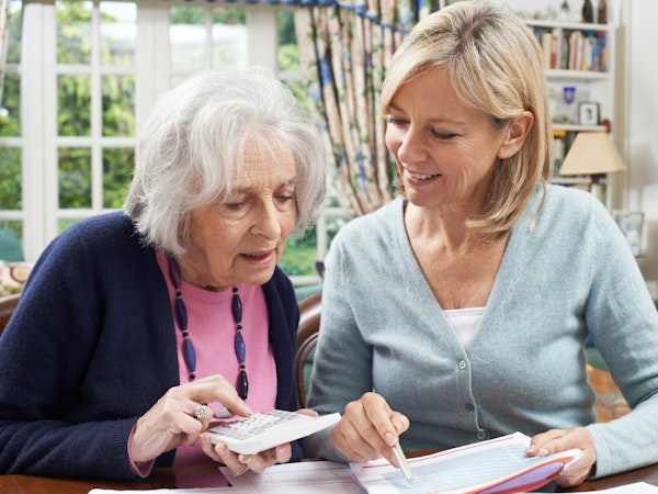 An senior woman holding a calculator and planning finances with a middle aged woman.