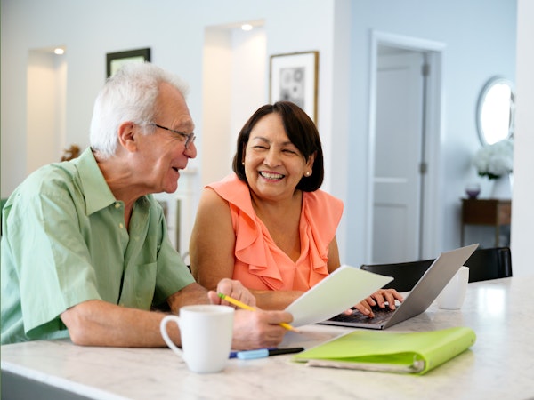 Older man and woman sitting at kitchen counter going through paperwork (Source: iStock)