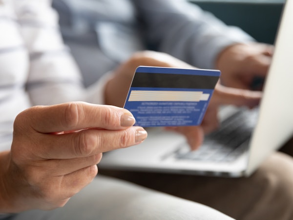Two older people looking at their credit card while on their laptop.