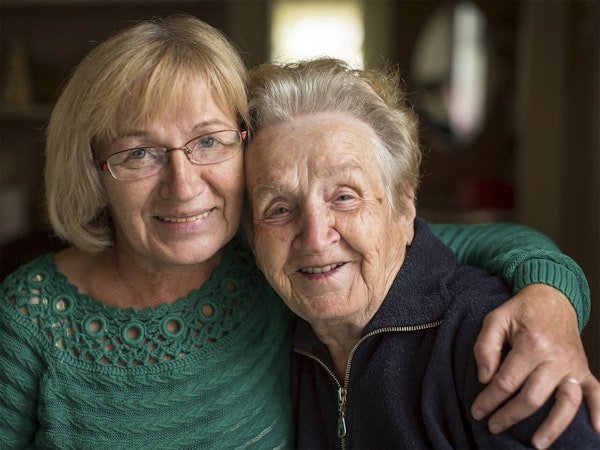Mature aged daughter with her arm around her elderly mother, both looking into the camera smiling (Source: Shutterstock)